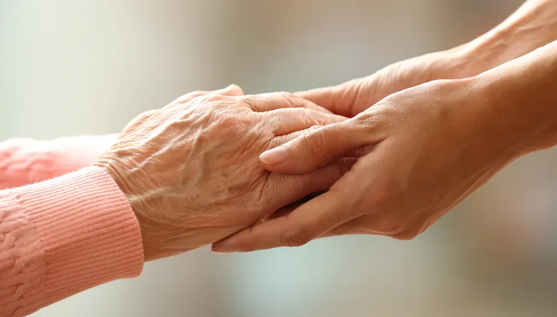 An older person's hand held gently by a younger hand