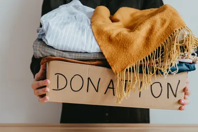 Woman holding a box of clothes for donation links to donation page